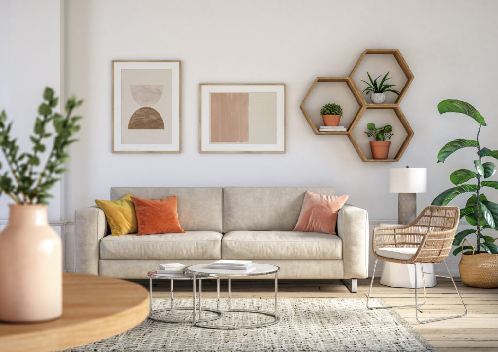 Modern living room with a beige sofa, orange and yellow cushions, abstract art on the wall, hexagonal shelves with plants, a wicker chair, and a floor lamp. A round wooden table with a vase and a rug complete the decor.